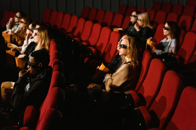 People wearing 3D glasses and eating popcorn in a cinema with red chairs. Granska publikens kvalitet